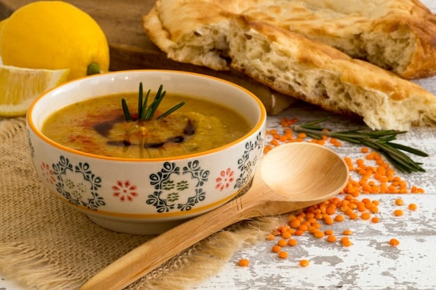 A close-up shot of a bowl of vibrant lentil soup, garnished with fresh herbs and a swirl of olive oil. The background shows a rustic kitchen setting, with a wooden spoon resting on a cutting board.