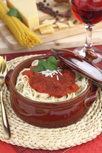 A close-up shot of a plate of spaghetti with homemade tomato sauce, garnished with fresh basil and a sprinkle of parmesan cheese. The background shows a warm and cozy dining room setting.