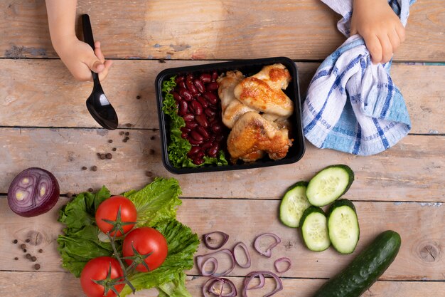 An overhead shot of hands carefully arranging various healthy food items into a divided lunchbox, including apple slices, carrot sticks, a small whole-wheat tortilla wrap with turkey and lettuce, a container of mixed berries, and a small portion of trail mix containing nuts and seeds, emphasizing portion control and variety.
