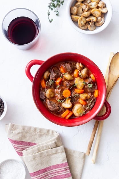 A close-up shot of a slow cooker filled with hearty beef stew. The stew is rich and thick, with chunks of beef, carrots, potatoes, and celery visible. The focus is on the texture and colors of the stew, emphasizing its warmth and comforting nature.