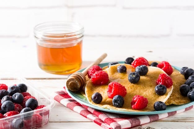 A stack of fluffy gluten-free pancakes topped with fresh berries and a drizzle of maple syrup, with a glass of orange juice in the background.