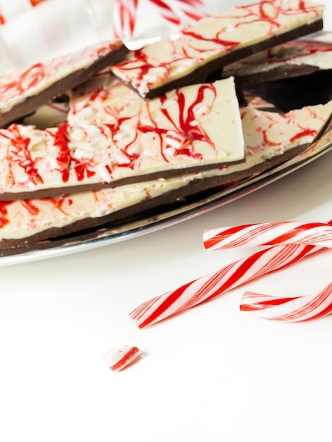 A close-up shot of chocolate peppermint bark, showing the layers of dark and white chocolate topped with crushed peppermint candies. The bark is arranged on a festive holiday platter.