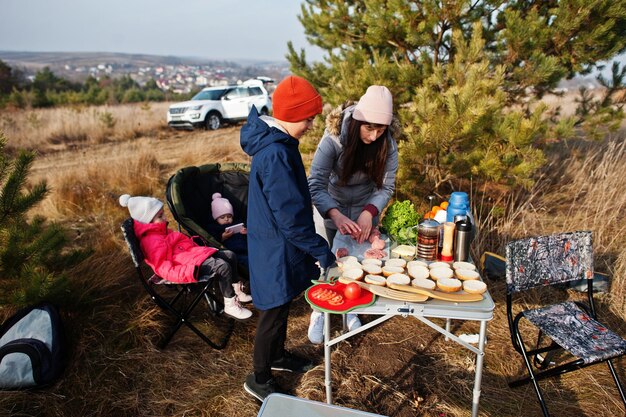 A family setting up a campsite with a tent, a picnic table with food, and a portable grill, illustrating a cost-effective and fun way to enjoy a road trip.