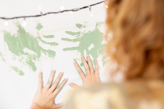 A close-up shot of a child's hands covered in paint, adding a brushstroke to a section of a family mural. Other family members' hands are visible in the background, also working on the mural.