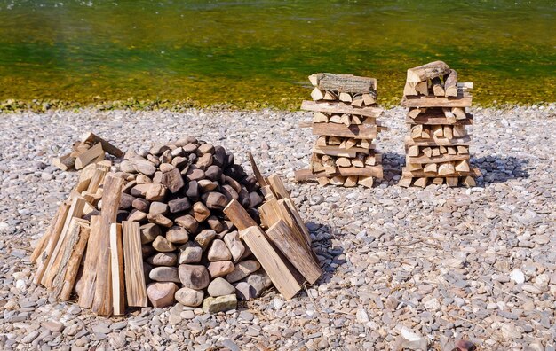 A close-up shot of various affordable fire pit materials, including concrete blocks, reclaimed bricks, and decorative gravel, arranged on a garden table. The sunlight highlights the textures and colors of the materials.