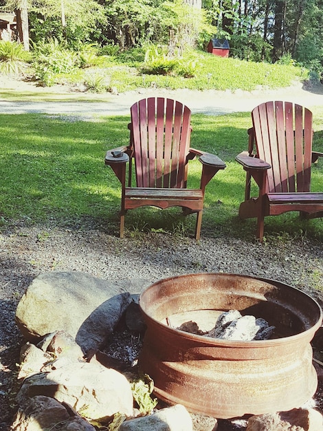 An eye-level shot of a personalized fire pit area. Comfortable Adirondack chairs are arranged around the concrete block fire pit. String lights are draped above, casting a warm glow. Soft blankets and pillows are placed on the chairs for added comfort.