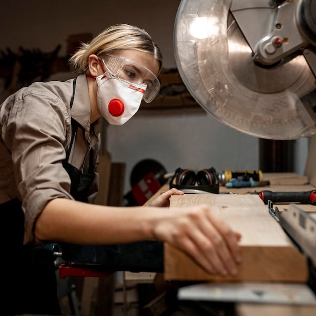 A person sanding a piece of wood with sandpaper in a well-lit workshop. Safety glasses and a dust mask are being worn.