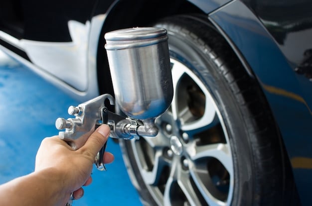 A close-up shot of a person painting a car tire with bright blue paint. They are using a small brush, and the tire rests on a tarp to protect the ground. The focus is on the vibrant color and the texture of the tire being painted.