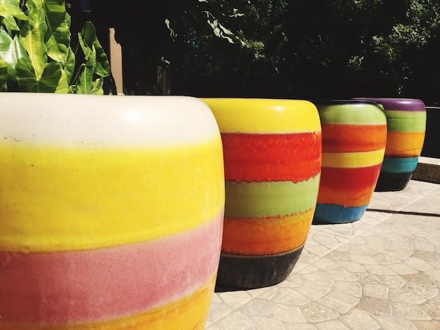 A collection of colorful tire planters arranged in ascending order of size, painted in bright, varied colors. Each tire is filled with different kinds of flowering plants, and they are placed on green grass. The sun is shining brightly, illuminating the rainbow of flower and painted tire colors.