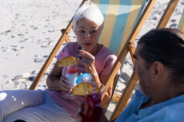 A happy caregiver is on the beach, sitting under an umbrella while reading a book. Nearby, drinks and sunscreen are sitting on a table, along with a small sandcastle.